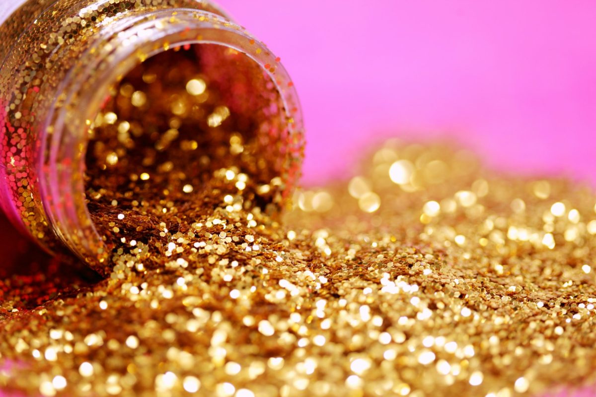 Gold glitter spilling from a jar across a bright pink surface