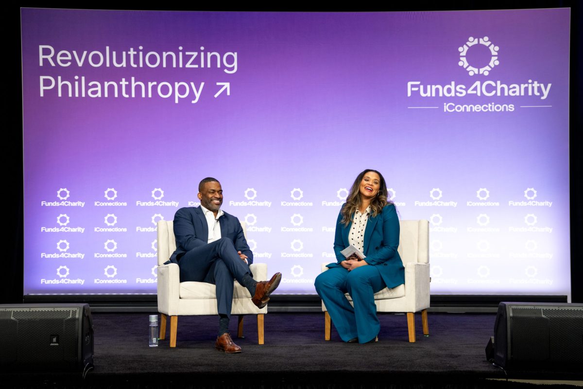 Two panellists seated on stage in front of a screen reading Revolutionizing Philanthropy