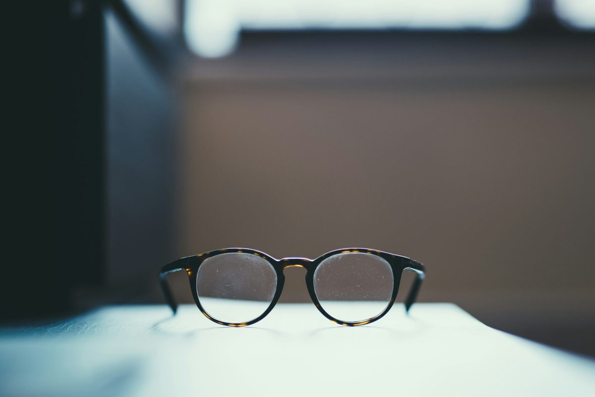 A pair of tortoiseshell reading glasses resting on a white table beside a window