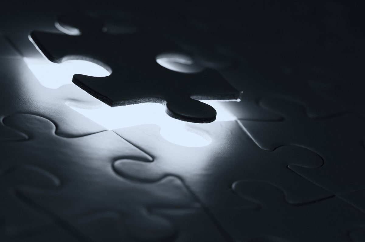 A single jigsaw piece lifted away from a dark puzzle, with light showing through the gap